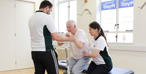 Elderly patient gets help standing; by two trained ManchesterOT therapists.
